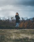 From below of pretty casual female in black coat with crossed arms feeling cold on autumn field — Stock Photo