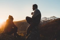 Silhouette entspannter Männer und Frauen, die bei Sonnenuntergang im Gegenlicht auf einem Berggipfel sitzen — Stockfoto