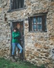 Lässige Frau in grünem Pullover steht mit verschränkten Armen neben Tür des alten Landhauses aus Stein — Stockfoto