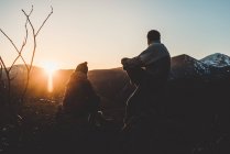 Silhouette d'homme et de femme détendus assis en contre-jour sur le sommet de la montagne au coucher du soleil — Photo de stock