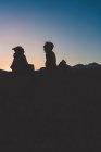 Silhueta de homem e mulher relaxados sentados em backlit no topo da montanha ao pôr do sol — Fotografia de Stock