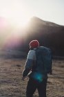 Back view of male backpacker in red knitted cap hiking in mountains on sunny autumn weather — Stock Photo