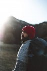 Side view of bearded male backpacker in red knitted cap hiking in mountains on sunny autumn weather — Stock Photo