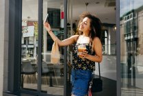 Femme ethnique joyeuse prenant selfie comme quitter le restaurant — Photo de stock
