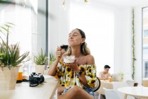 Stilvolle Frau beim Essen und Lesen von Büchern im Café, Menschen im Hintergrund — Stockfoto