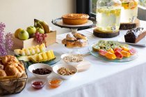 Вид сбоку на праздничный ужин с вкусной фруктовой выпечкой и стильными банками лемонады на столе, украшенном цветами лилака — стоковое фото