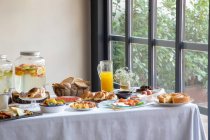 Desde arriba de la mesa de estar apetitosa para el desayuno con sándwiches de marisco panadería y zumo de naranja en el elegante comedor. - foto de stock