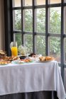 Зверху апетитний стіл для сніданку з хлібобулочними виробами сендвічі та апельсиновий сік у стильній їдальні — стокове фото