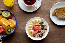 Зверху миска граноли зі смачними ягодами та бананом подається на стіл з тарілкою фруктів та чашкою чаю зі сніданком — стокове фото