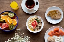 Von oben Schüssel Müsli mit leckeren Beeren und Banane auf dem Tisch serviert mit Teller mit Obst und Teetasse mit zum Frühstück — Stockfoto