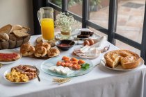 From above of appetizing sitting table for breakfast with bakery seafood sandwiches eggs and orange juice at stylish dinning room. — Photo de stock