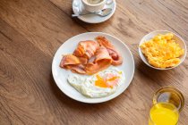 Сверху свежие жареные яйца с беконом в тарелке, подаваемые на завтрак с соком и кофе — стоковое фото