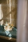 Bando de delicadas flores brancas colocadas na almofada rústica azul perto da janela em casa — Fotografia de Stock