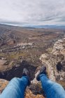 Piedi di persona in jeans seduti sul bordo della montagna con vista mozzafiato sulla valle panoramica — Foto stock