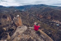 Сзади вид неузнаваемого человека в куртке, смотрящего и сидящего на вершине горы — стоковое фото