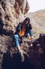 Спокійна жінка в теплому одязі спирається на руку і сидить на гірській скелі — стокове фото