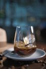 Вкусный ароматный коричневый напиток в стакане на круглом блюдце среди жареных кофейных зерен рядом со шляпой на глянцевом столе — стоковое фото