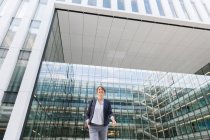Niedriger Winkel der entzückten Geschäftsfrau lächelt und geht vor zeitgenössisches Bürogebäude mit Glaswand — Stockfoto