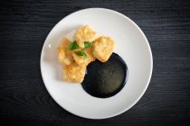 Merluza empanada con crema de calamar en plato - foto de stock