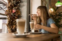 Blonde happy young female with bangs smiling and talking on smartphone while holding cup of coffee in cozy cafe — Stock Photo