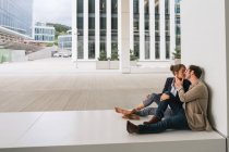 Masculino gerente abraçando e beijando mulher enquanto sentado fora escritório edifício no cidade rua depois do trabalho — Fotografia de Stock