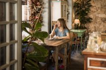 Блондинка счастливая молодая женщина с челкой улыбается и разговаривает по смартфону в уютном кафе — стоковое фото