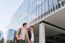 From below happy couple coworkers holding hands smiling and walking together outside modern building — Stock Photo
