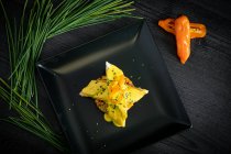 Corvina with yellow pepper sauce in black plate — Stock Photo