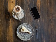 Blank screen smartphone next to coffee and cake on plate with ornament on wooden table — Stock Photo