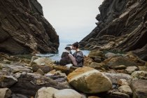 Mujer viajera besando perro sentado en la costa de roca - foto de stock