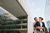 From below happy couple coworkers hugging while standing outside modern building on city street after work — Stock Photo