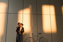 Бизнесмен обнимает и целует подружку, стоя рядом с велосипедом возле современного здания после работы — стоковое фото
