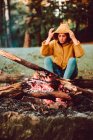 Mulher viajante aquecendo as mãos perto de fogueira na clareira da floresta — Fotografia de Stock