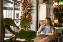 Blonde happy young female with bangs smiling and talking on smartphone in cozy cafe — Stock Photo