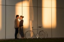 Бізнесмен обіймає дівчину, стоячи біля велосипеда за межами сучасної будівлі після роботи — стокове фото