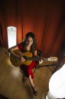 Von oben talentierte Frau in rotem Kleid singt und spielt Gitarre in warm beleuchteter Bühne neben weißer Lampe — Stockfoto