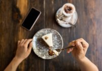 Female holding fork with cake sitting at table with blank screen smartphone next to coffee — Stock Photo