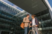 Fröhlicher Mann und Frau mit Fahrrad lächeln und schauen einander an, während sie vor dem Bürogebäude kommunizieren — Stockfoto