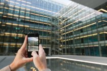 Male hands photographing with smartphone transparent glass facade of contemporary high rise business center in downtown — Stock Photo