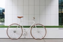Bicicleta estacionada na calçada perto da parede do edifício contemporâneo no dia ensolarado na rua da cidade — Fotografia de Stock