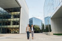 From below happy couple coworkers holding hands and walking together outside modern building on city street after work — Stock Photo