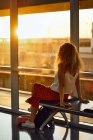 Stilvolle, fröhliche Frau sitzt auf einer Metallbank im gläsernen Flur des Flughafens in Texas — Stockfoto