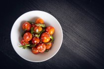Зверху смачні апетитні вишневі помідори, обсмажені зеленою спаржею та розмарином у білій тарілці на сірому фоні — стокове фото