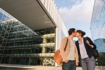 From below happy couple coworkers kissing each other while standing outside modern building on city street after work — Stock Photo