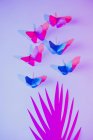Рожеві і сині метелики прикріплені до бузкової стіни над різьбленим паперовим листом — стокове фото