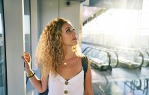Charming curly woman with backpack walking along light spacious room of airport in Texas — Stock Photo