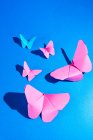 Хрупкие розовые бабочки из бумаги и прикрепленные к голубой шелковой ткани — стоковое фото