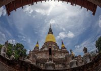 De baixo do templo budista antigo com estátuas na jarda contra o céu nublado no dia ensolarado na Tailândia — Fotografia de Stock