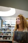 Content curly woman looking away walking between bookshelves in library of Texas — Stock Photo