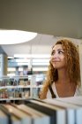 Mujer rizada contenta mirando hacia otro lado caminando entre estanterías en la biblioteca de Texas - foto de stock